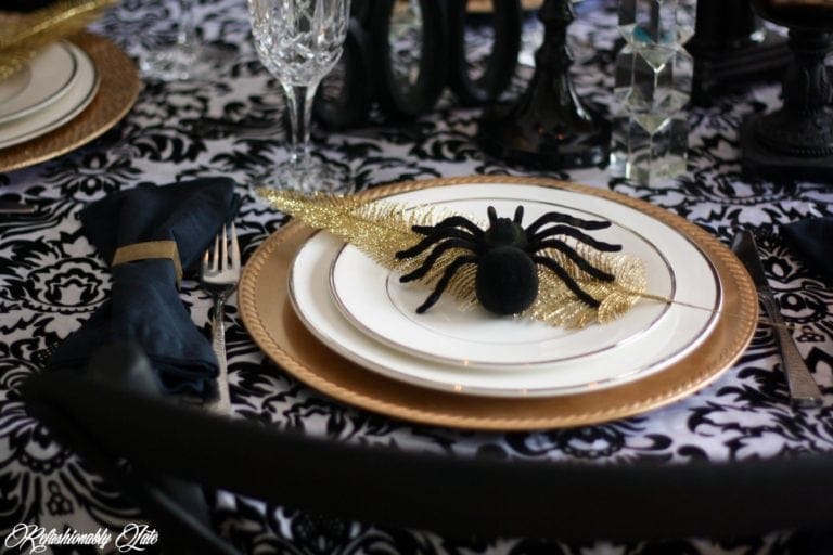 Spider sitting on top of a white china and a gold charger on a damask tablecloth