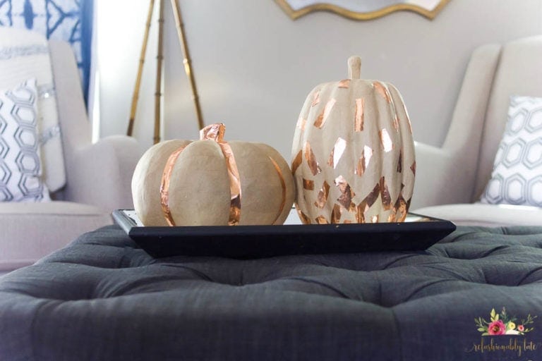 two paper mache pumpkins with copper washi tape decorations on an ottoman