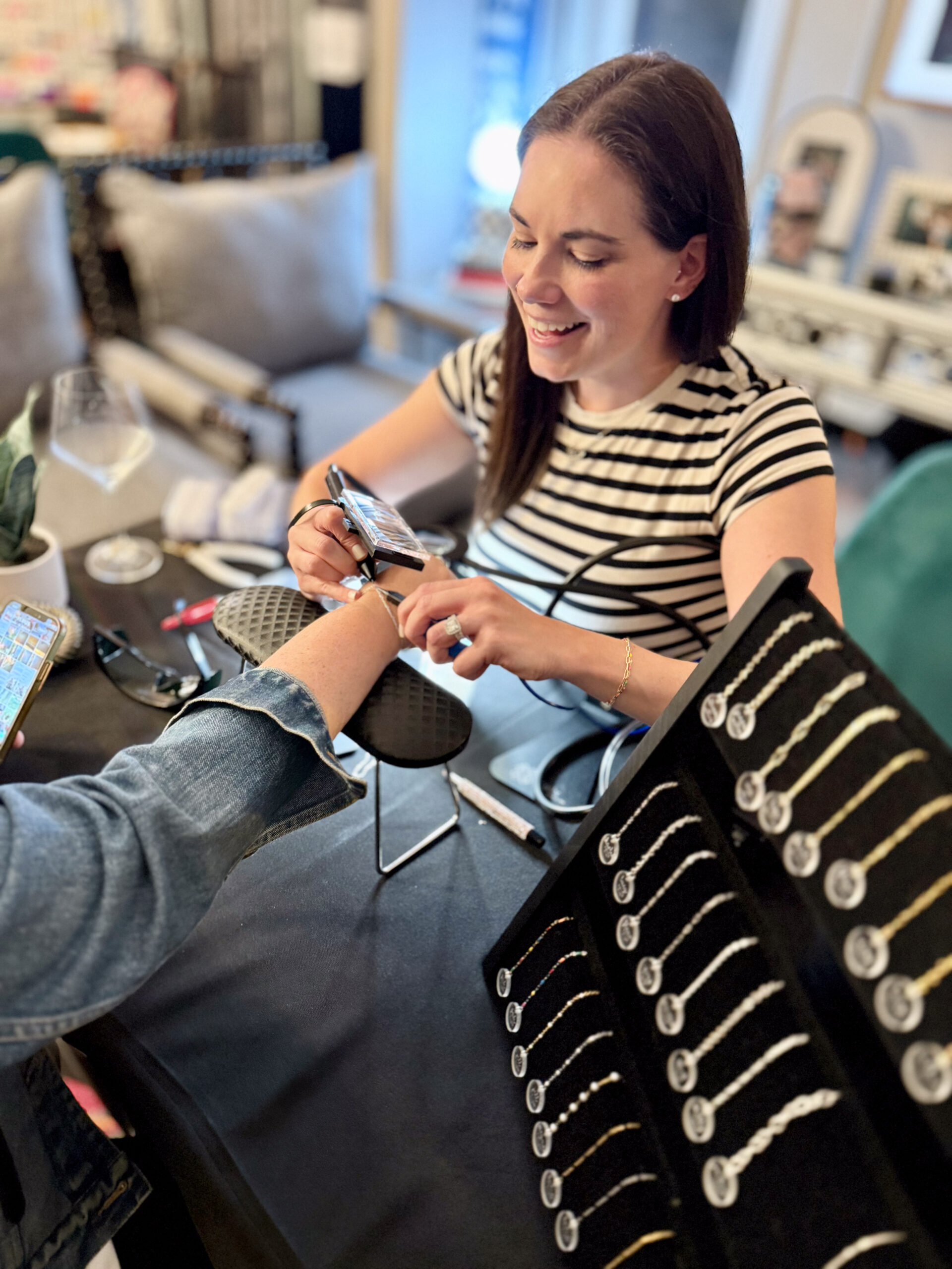 Permanent jewelry Minneapolis – Ruthie welding a custom permanent bracelet for a client while showcasing gold-filled and sterling silver chains at a permanent jewelry event.