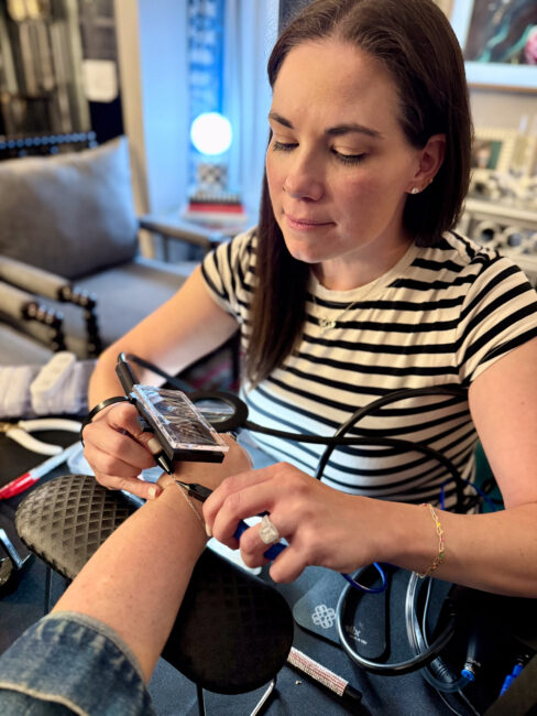 Ruthie welding a custom permanent bracelet on a client using a micro welder, creating permanent jewelry in Minneapolis with gold-filled and sterling silver chain options.