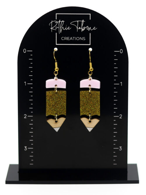 Handmade pencil dangle earrings with pink erasers, gold glitter acrylic, natural wood tips, and gold hooks displayed on a Ruthie Tabone Creations earring size guide.