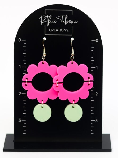 Hot pink flower dangle earrings with mint green accents displayed on a black measurement stand, highlighting their bold contrast, playful shape, and approximate drop length for easy size reference.