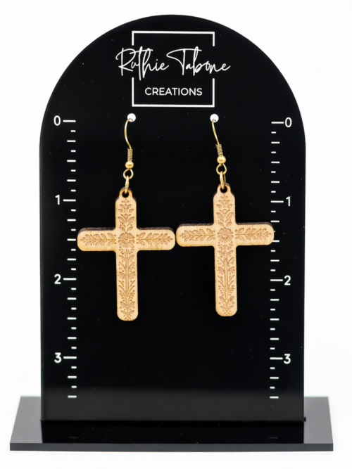 Wood cross dangle earrings with engraved floral detail and gold hooks, displayed on a black Ruthie Tabone Creations earring card with measurement markings.