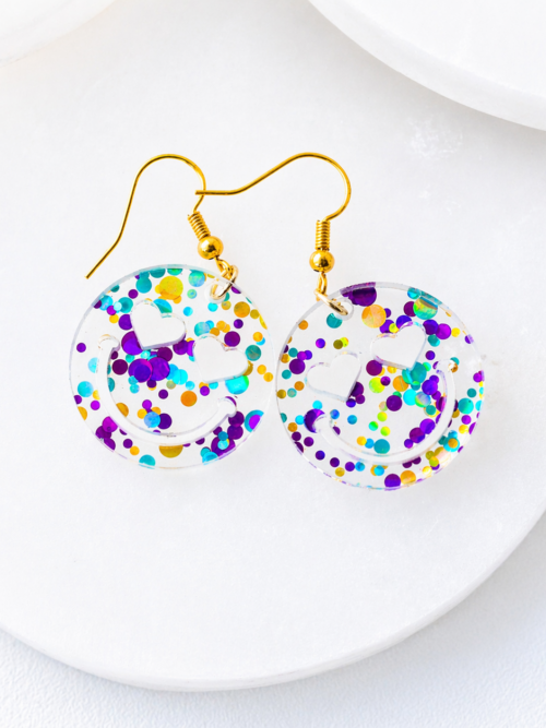 Clear acrylic smiley face dangle earrings with colorful confetti and heart-shaped eyes, finished with gold hooks, displayed on a clean white background.
