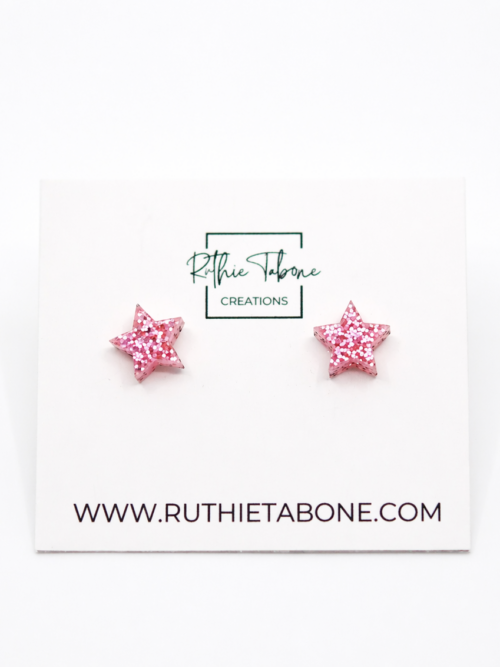 Pink glitter star stud earrings displayed on a Ruthie Tabone Creations card with a clean white background.