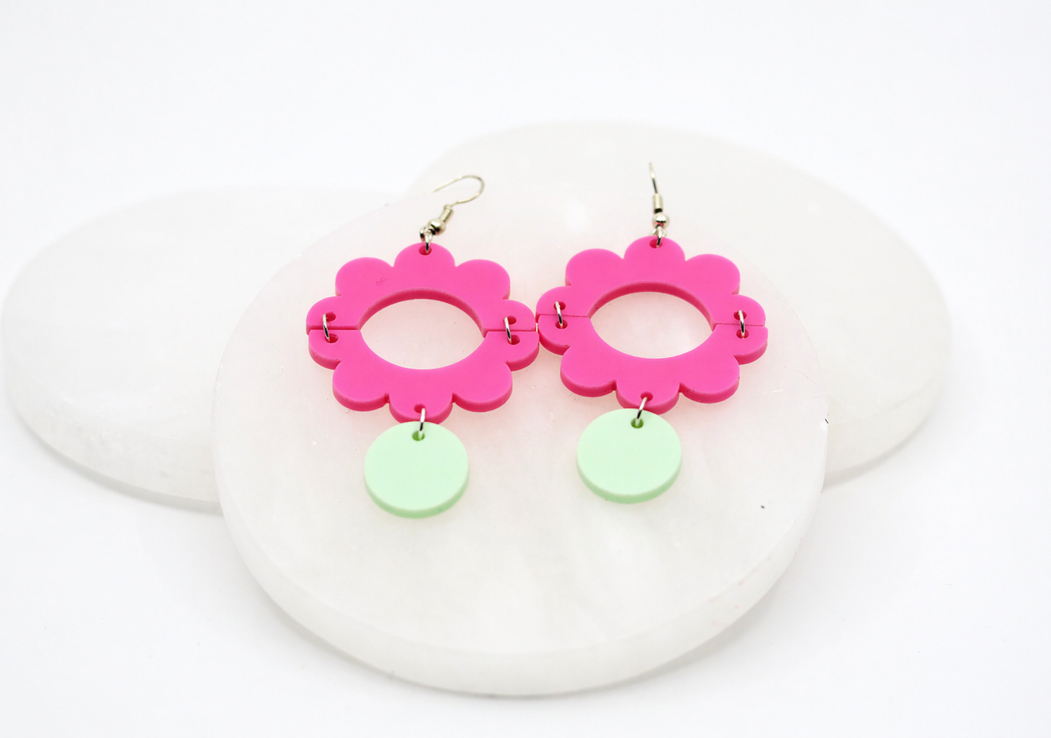 Bright pink acrylic flower dangle earrings featuring a playful cutout design with a soft mint green accent drop, styled on a clean white stone background for a fun, bold, and modern look.