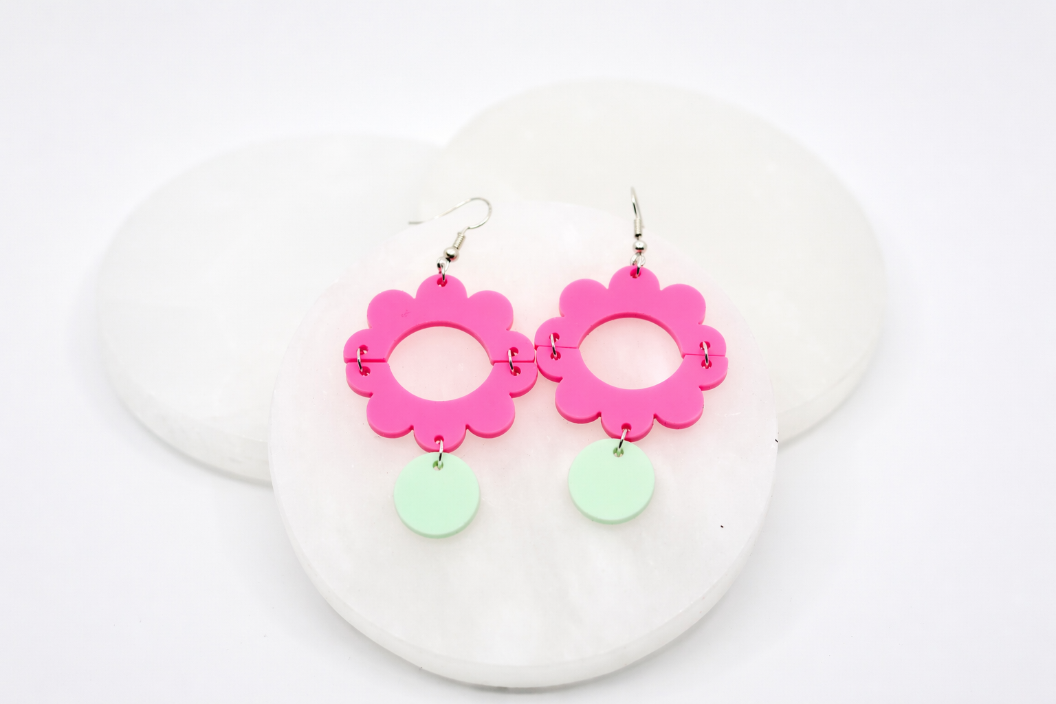 Hot pink acrylic flower dangle earrings with a bold open-center design and soft mint green drop accents, styled on a white stone background for a bright, playful, and modern statement look.