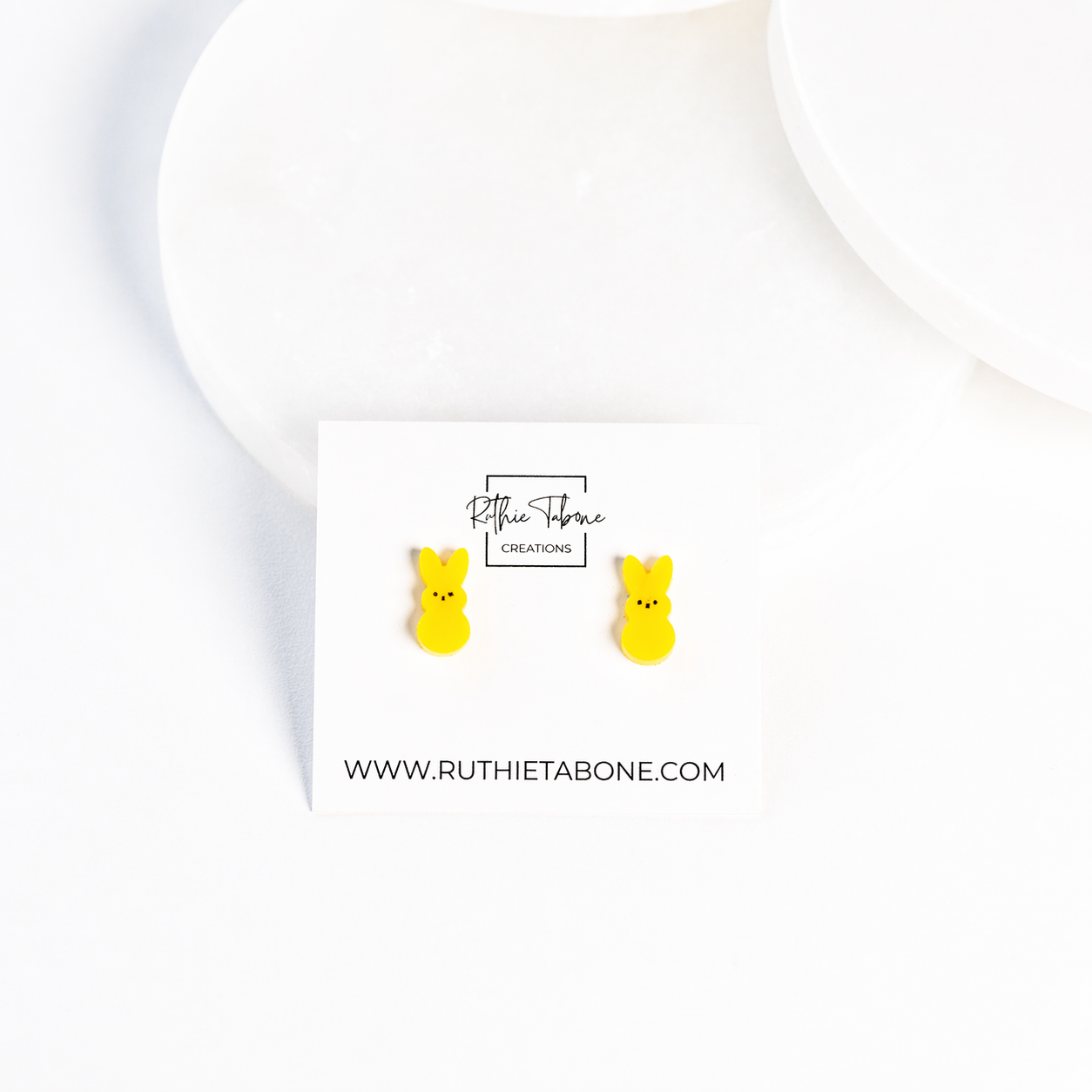 Yellow bunny stud earrings displayed on a branded Ruthie Tabone Creations card, styled on a clean white background with soft, minimal props.