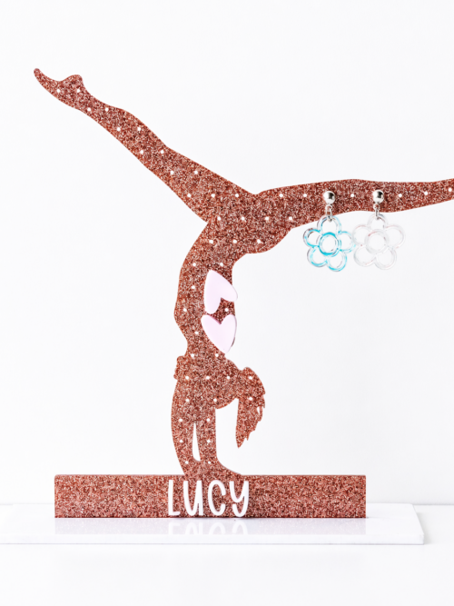Glitter gymnast silhouette earring holder personalized with the name “Lucy,” displaying small flower stud earrings against a clean white background.