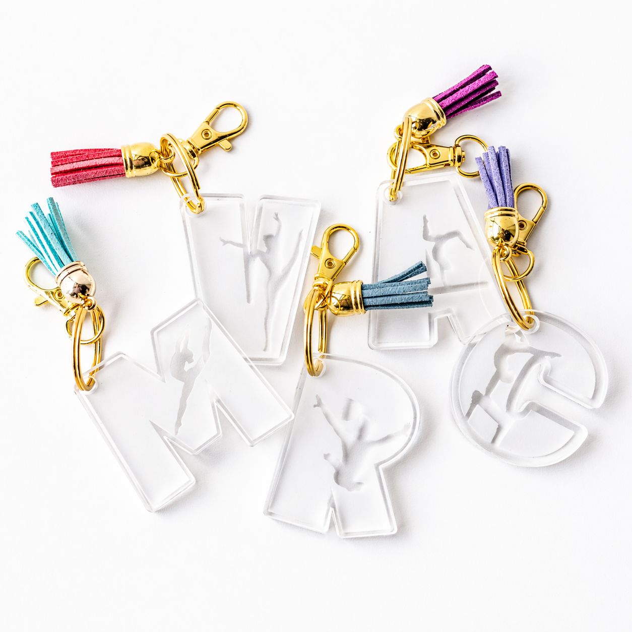 Personalized gymnast acrylic keychains in multiple letter styles, featuring clear engraved designs with gymnast silhouettes, gold hardware, and colorful tassels—perfect for customizing names, team gifts, and gym bags with a fun, sporty touch.