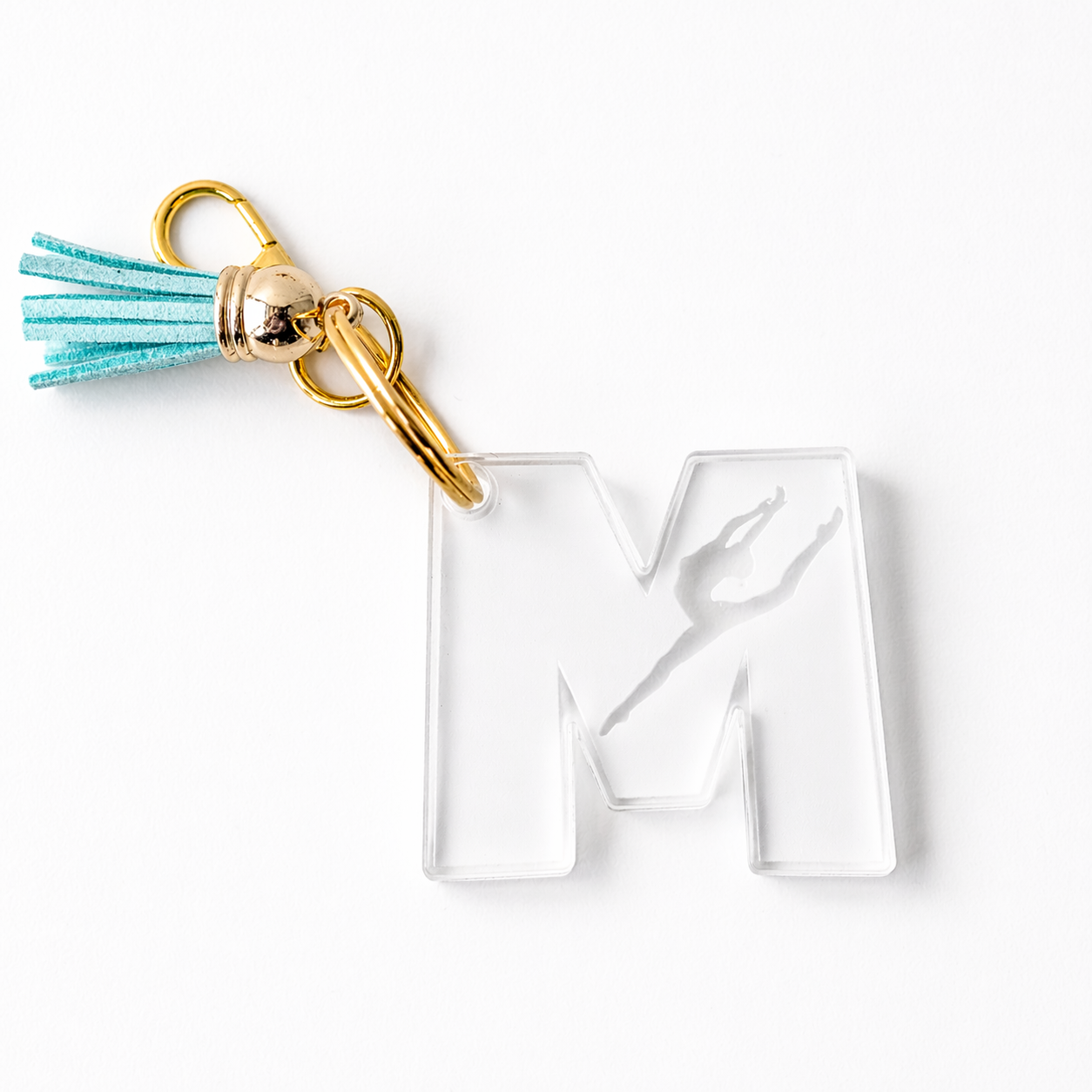 Personalized gymnast “M” acrylic keychain featuring a clear engraved design with a gymnast silhouette, accented with gold hardware and a teal tassel—perfect for gym bags, backpacks, or a thoughtful custom gift for gymnasts and dance lovers.