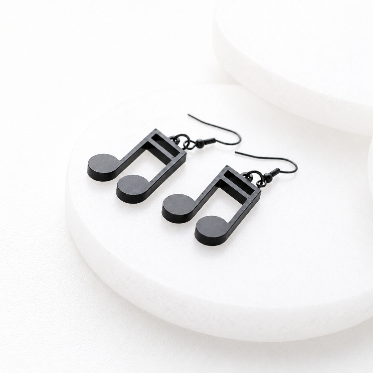 Black music note dangle earrings with hook backs on a white minimalist background