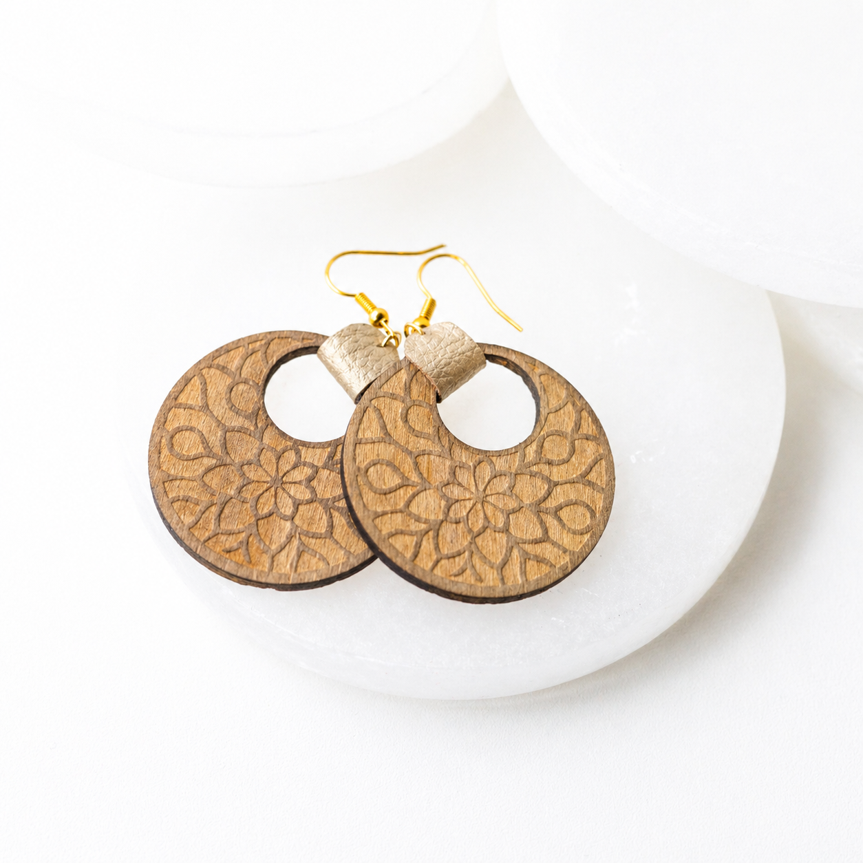 Wood mandala earrings with engraved floral design and gold hook backs on white display