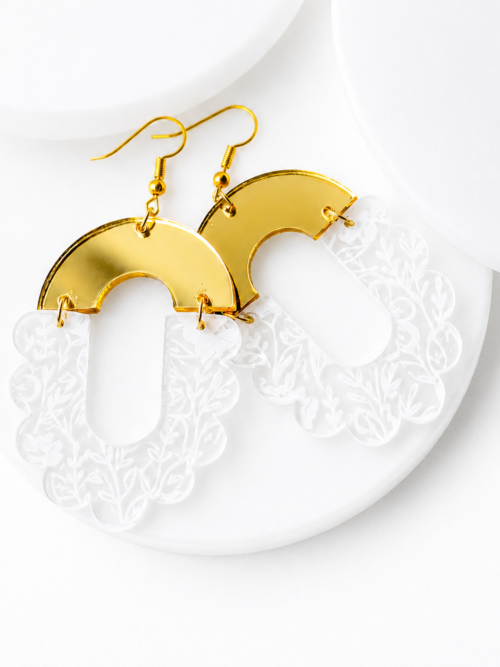 White floral engraved acrylic statement earrings with gold mirror acrylic tops and gold hypoallergenic hooks, displayed on a white textured background. These lightweight geometric dangle earrings feature a scalloped floral design with elegant gold accents for a modern boho style.