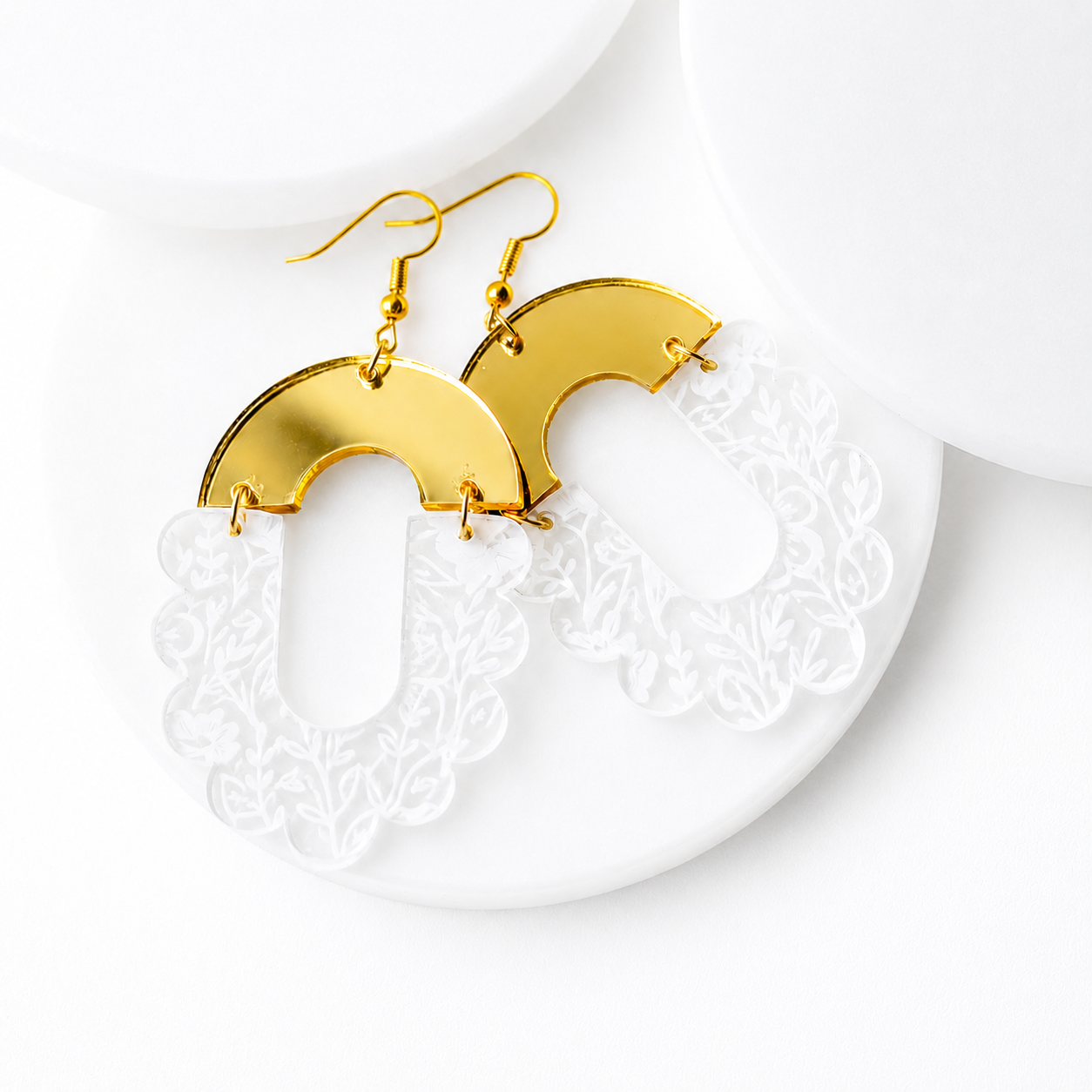 White floral engraved acrylic statement earrings with gold mirror acrylic tops and gold hypoallergenic hooks, displayed on a white textured background. These lightweight geometric dangle earrings feature a scalloped floral design with elegant gold accents for a modern boho style.