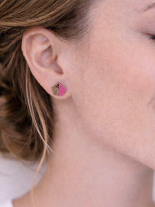 Close-up of a woman wearing a handmade geometric pink and natural wood stud earring with a modern pentagon shape.