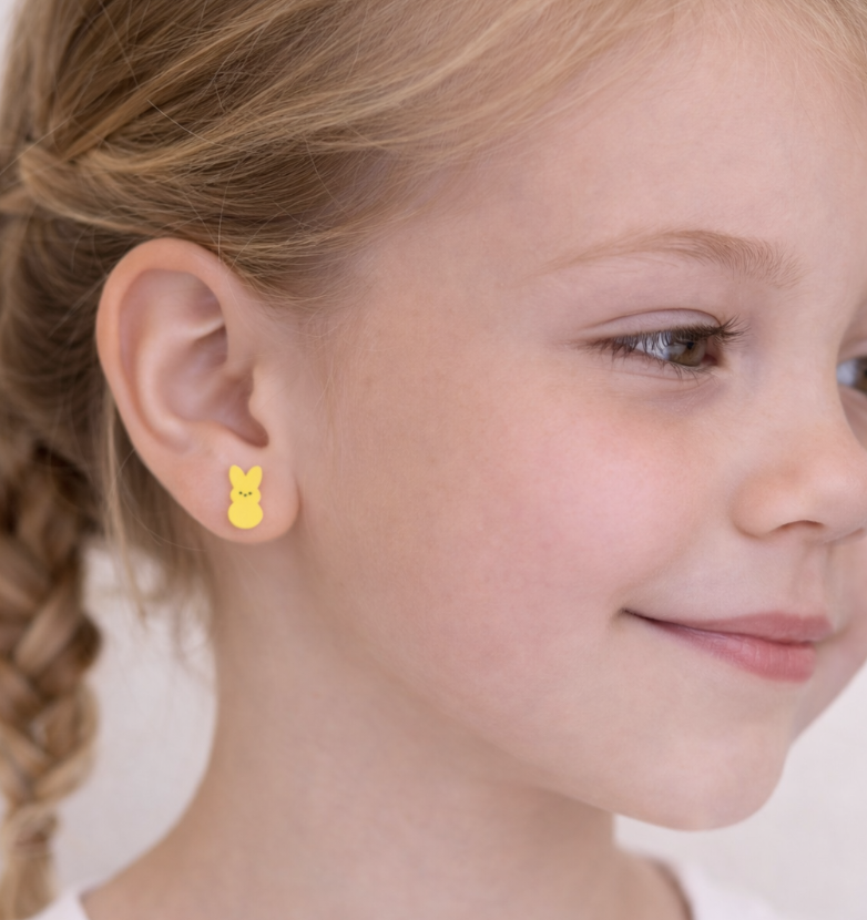 Child wearing yellow bunny stud earrings, shown in a close-up side profile with braided hair and a soft, natural background.