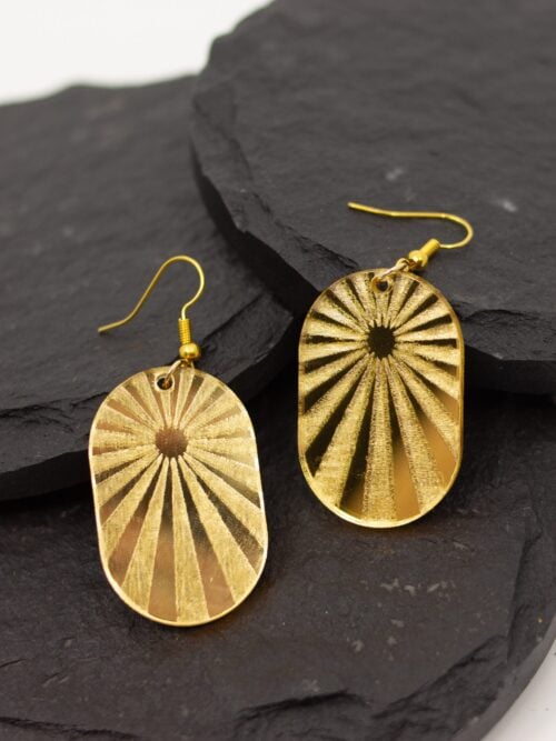 Handmade gold mirrored acrylic sunburst arch earrings with hypoallergenic hooks displayed on layered black slate stones.