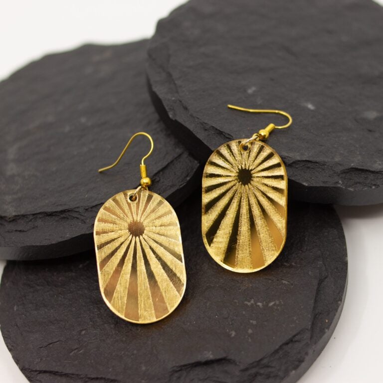 Handmade gold mirrored acrylic sunburst arch earrings with hypoallergenic hooks displayed on layered black slate stones.