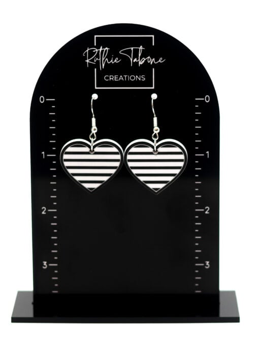 Black and white striped heart dangle earrings with silver hooks displayed on a black Ruthie Tabone Creations earring card with measurement markings.