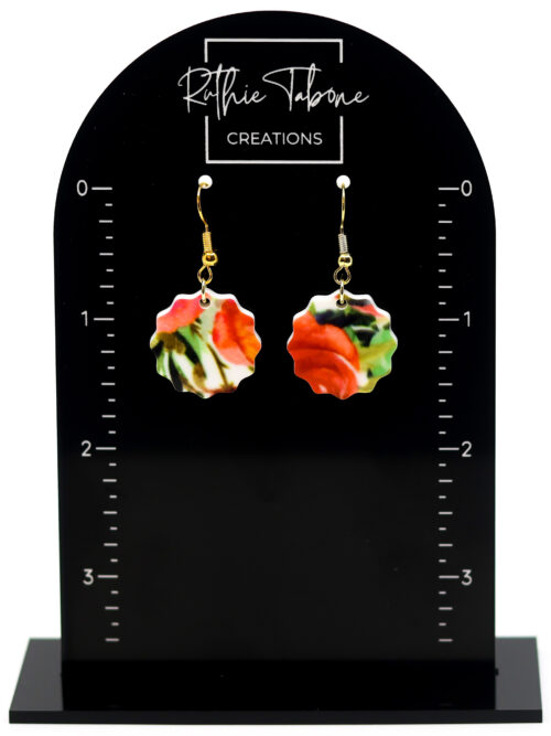 Red floral scalloped acrylic dangle earrings with gold hooks displayed on a black Ruthie Tabone Creations earring card with measurement markings.