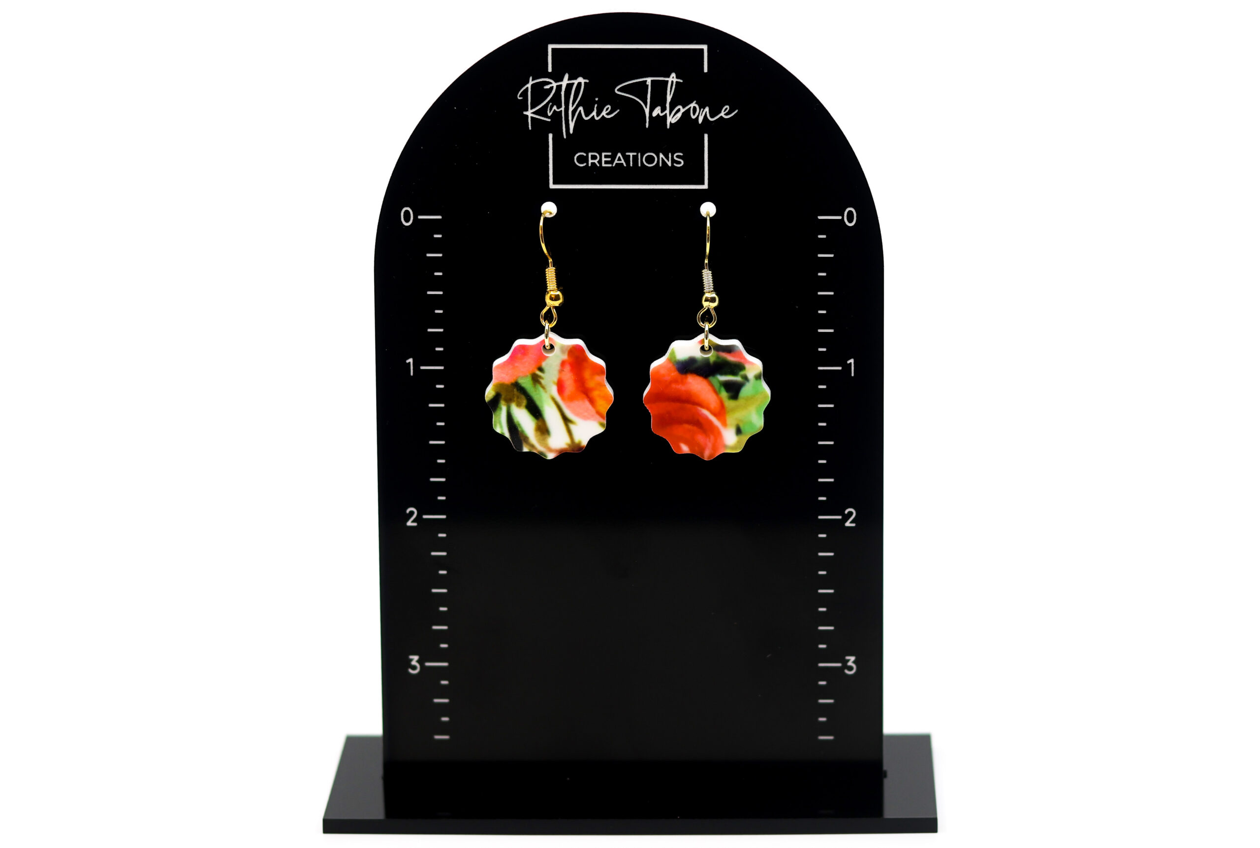 Red floral scalloped acrylic dangle earrings with gold hooks displayed on a black Ruthie Tabone Creations earring card with measurement markings.