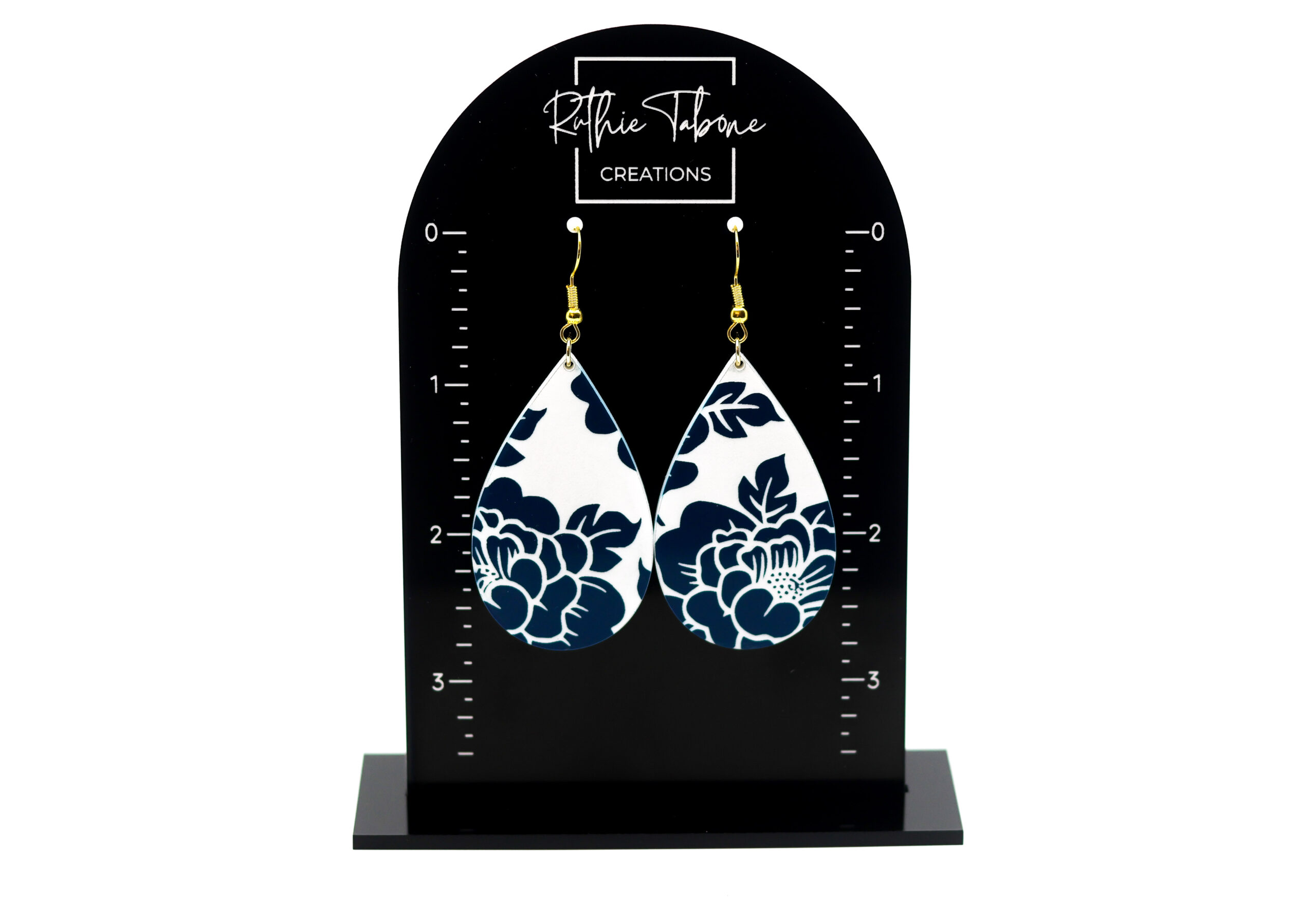 Navy blue floral teardrop dangle earrings displayed on a branded earring stand, featuring a crisp white background and gold hooksβlightweight, elegant, and perfect for adding a classic pop of pattern to any outfit.