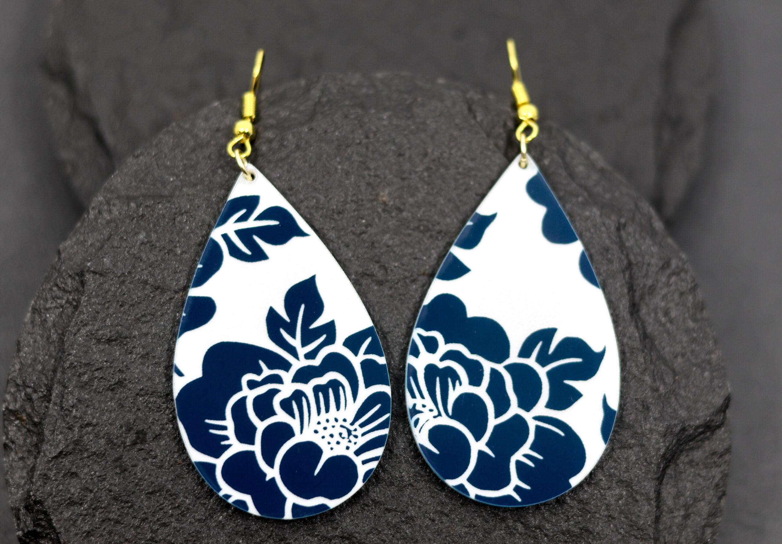 Teardrop-shaped earrings featuring a bold blue floral pattern on a crisp white background, finished with gold hooksβlightweight, eye-catching, and perfect for adding a pop of pattern to any outfit.