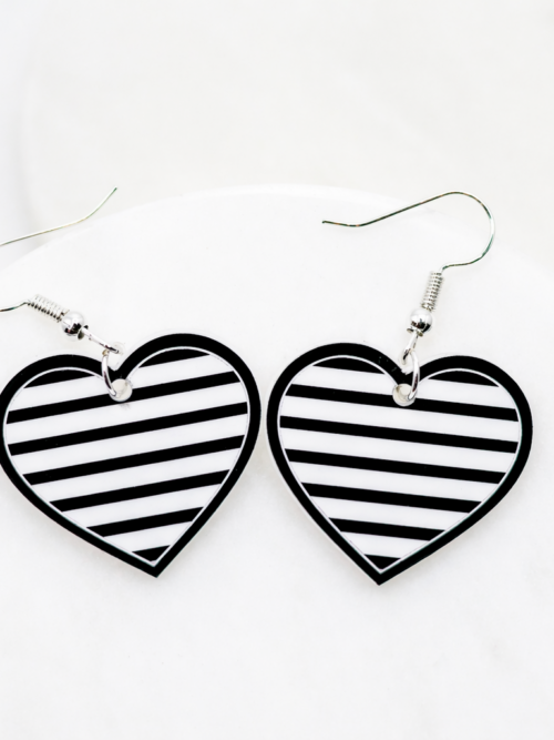 Black and white striped heart acrylic dangle earrings with silver hooks, displayed on a clean white background.