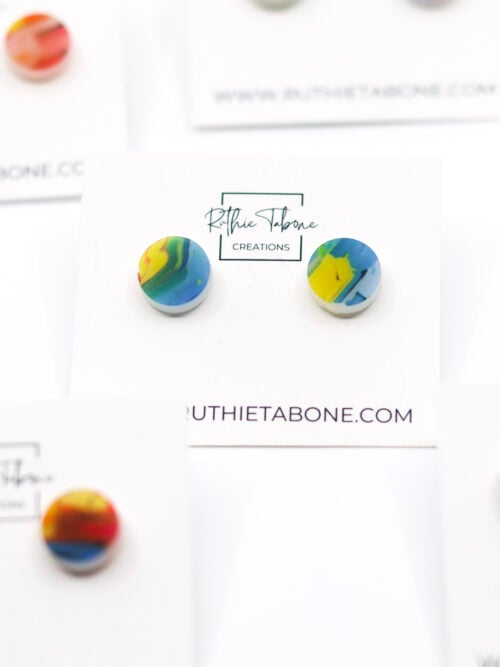 Colorful round acrylic stud earrings with a marbled rainbow design, displayed on Ruthie Tabone Creations cards with multiple pairs styled in the background.