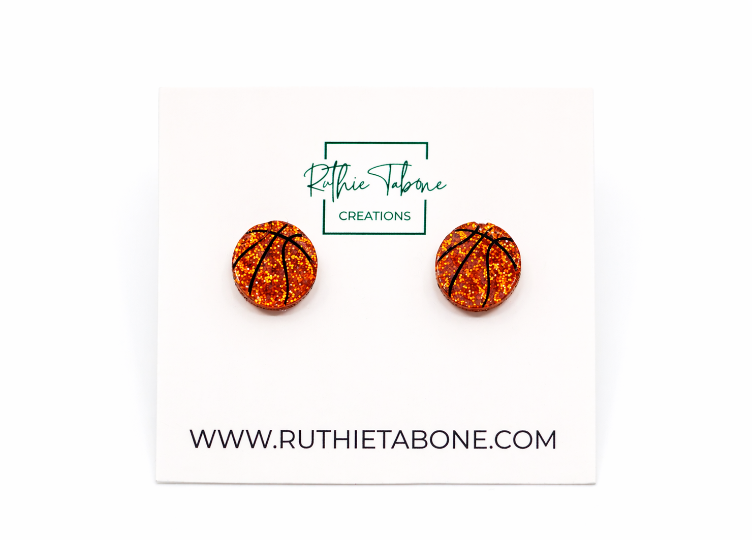 Glitter basketball stud earrings with black line detailing on a Ruthie Tabone Creations display card, shown on a clean white background.