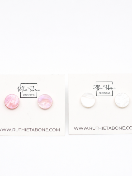 Two pairs of round stud earrings—one in pink marbled acrylic and one in white marbled acrylic—displayed on Ruthie Tabone Creations cards against a clean white background.