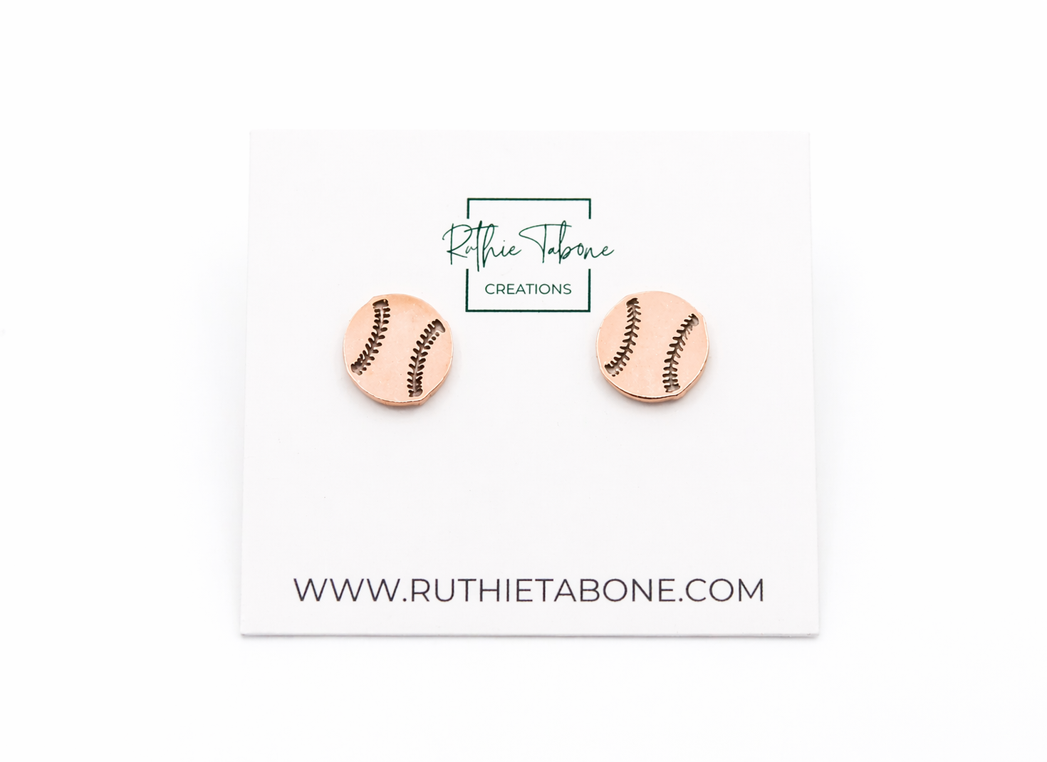 Rose gold baseball stud earrings displayed on a branded Ruthie Tabone Creations card, featuring a round design with engraved black stitching details for a sporty, minimalist look.