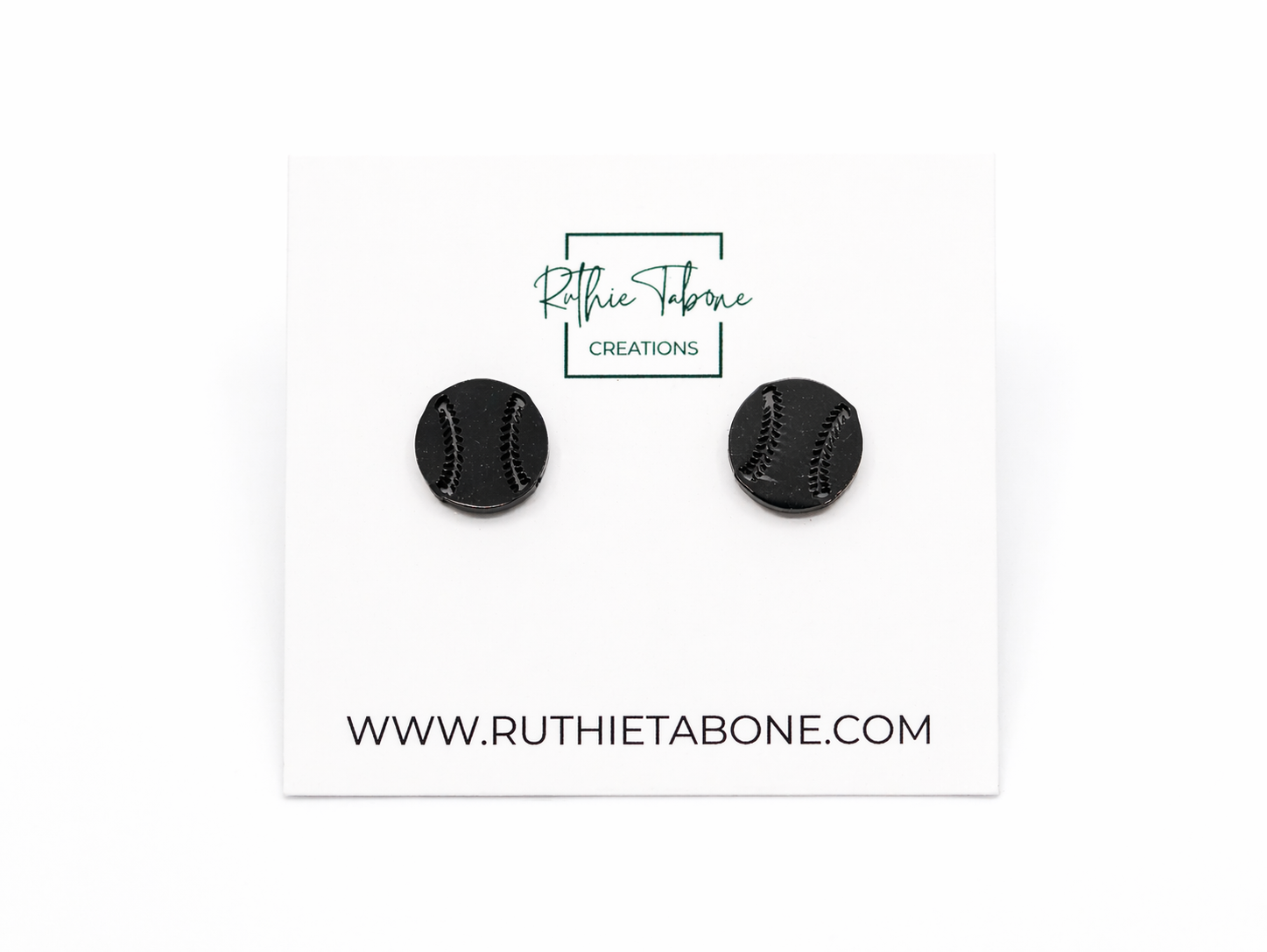 Black baseball stud earrings displayed on a branded Ruthie Tabone Creations card, featuring a round design with engraved black stitching details for a sporty, minimalist look.