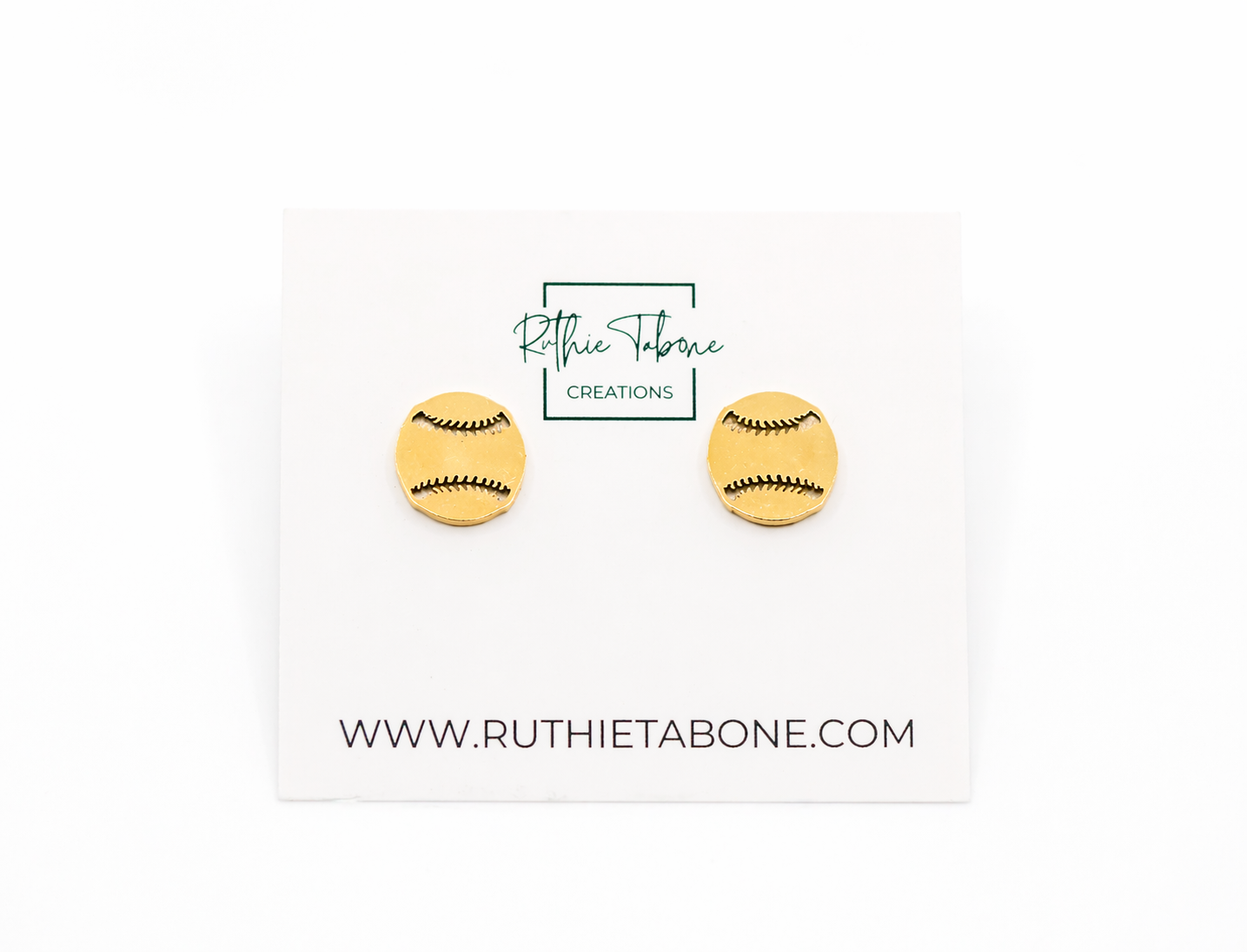 Gold baseball stud earrings displayed on a branded Ruthie Tabone Creations card, featuring a round design with engraved black stitching details for a sporty, minimalist look.