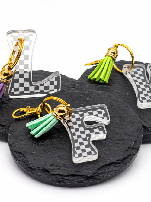 Clear acrylic checkerboard initial keychains with gold hardware and colorful tassel accents—modern, fun, and perfect for personalizing bags or keys.