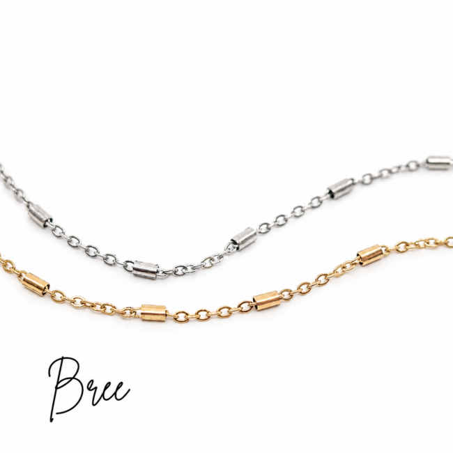 Close-up of two minimalist chain necklaces displayed on a bright white background. One necklace features polished silver links with evenly spaced cylindrical accents, while the other showcases the same design in gold. The timeless, versatile chains are ideal for everyday wear, layering, or permanent jewelry.
