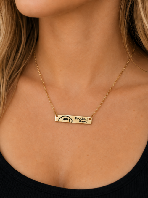 Gold Football Mom engraved bar necklace modeled on a woman, featuring a football design and delicate gold chain for sports moms and game day jewelry.